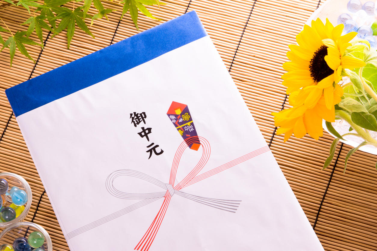 お中元ののし紙を付けた化粧箱と傍らにひまわりの花