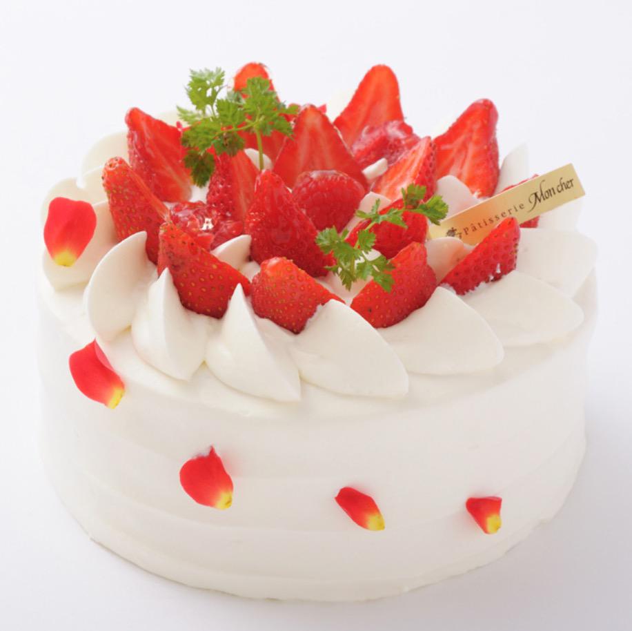 白い背景に置かれたいちごと花びらがあしらわれた豪華なホールケーキ