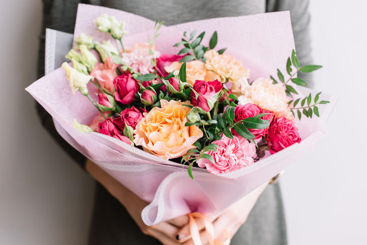 グレーのワンピースを着た女の人が持つバラ、カーネーション、トルコギキョウ、牡丹などのピンクの花束