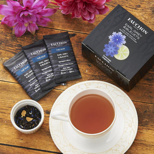 花が描かれた黒色のボックス、個包装のティーバッグが3つ、紅茶入りのカップ、ピンク色の花がテーブルの上に置かれている。