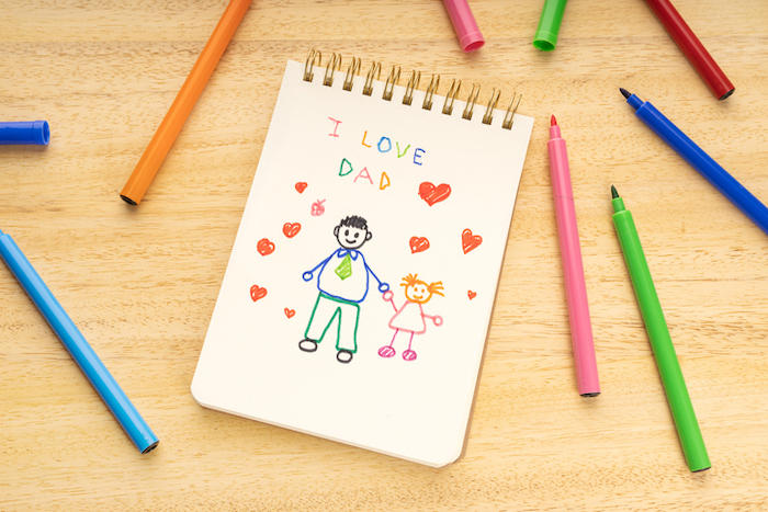 父親と子供の絵が描かれたノートの周りに、複数のカラーペンが散らばっている。