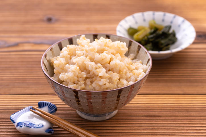 木製テーブルの上のお茶碗に盛られた玄米ご飯と豆皿に乗った漬物と箸置きと箸