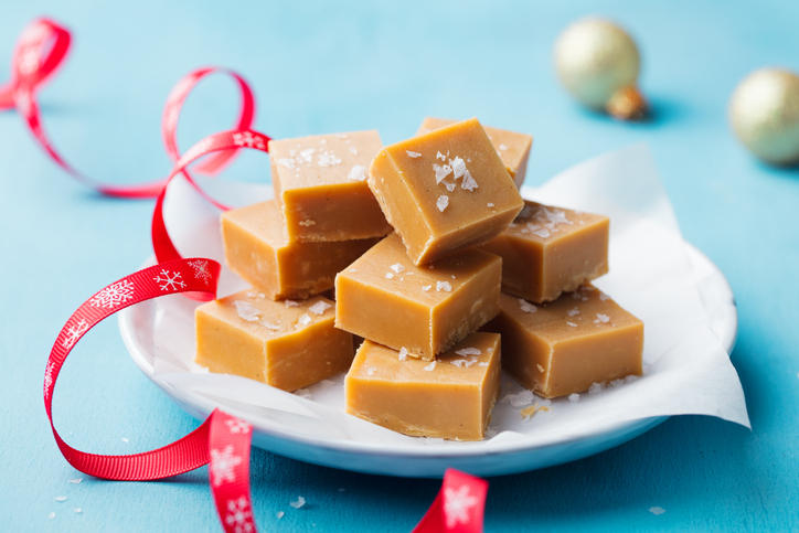 キャラメルは、青の背景にクリスマス赤リボン付きプレートにキャンディーをごまかします。クローズ アップ。 - クリスマスのロイヤリティフリーストックフォト