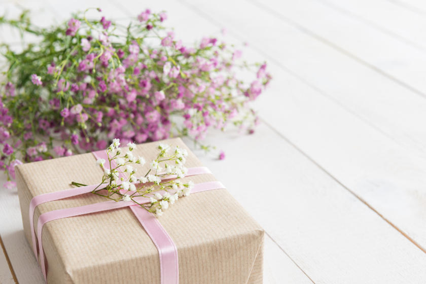 白い木製のテーブルに花とプレゼントが置かれている。