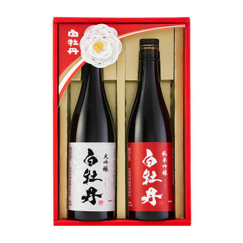 白椿の飾りがついた赤い化粧箱に、紅白のラベルがついた黒い日本酒ボトル2本が詰め合わせになっている