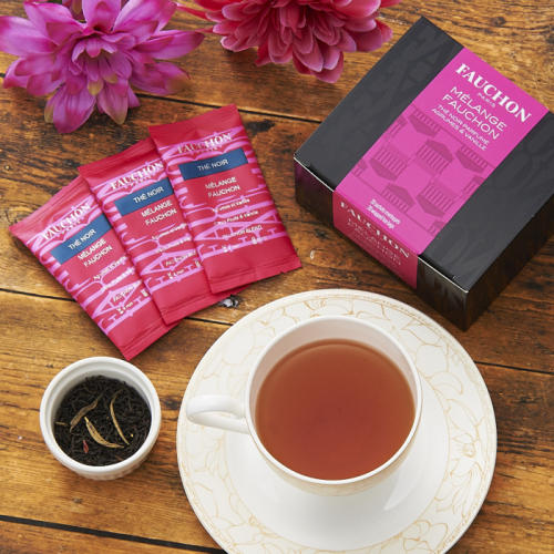 黒色のボックス、ピンク色のティーバッグのパッケージ3つ、紅茶入りのカップ、ピンク色の花がテーブルの上に置かれている。