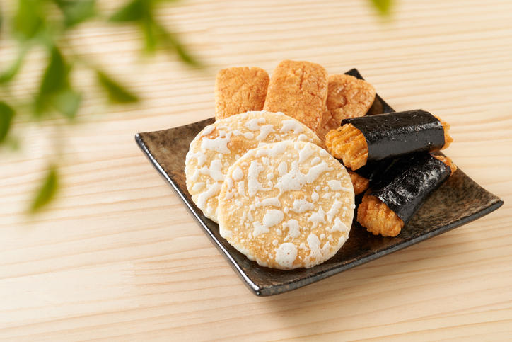 木のテーブルに置かれた黒い角皿にのったせんべい