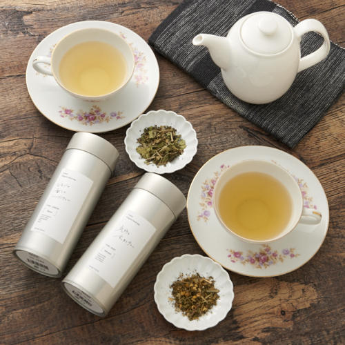 ハーブティーが入ったティーカップが2つ、シルバーの茶筒が2つ、ティーポットが1つ置かれている。