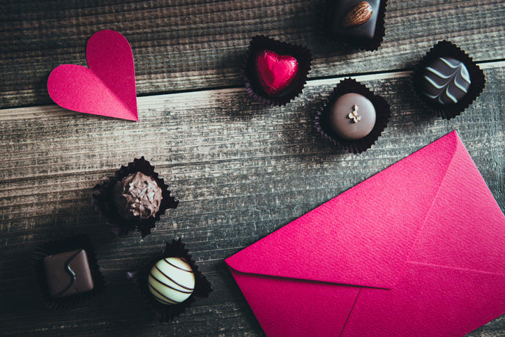 木製のテーブルに並んだチョコレート数粒と、ピンク色の封筒とハートの紙型
