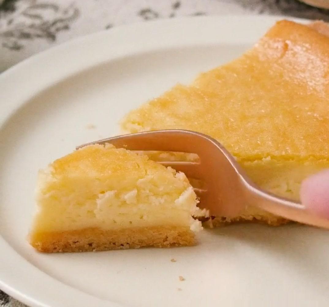 白い丸皿に乗った1ピースのチーズケーキがフォークで切られている様子