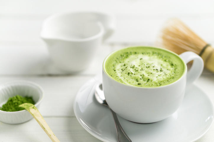 抹茶ラテが入った白いティーカップが置かれ、周りには茶せんや抹茶が置かれている。