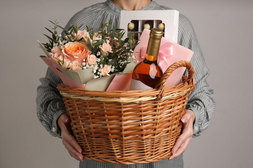 女性が、ワインや花が入った木のバスケットを持っている。