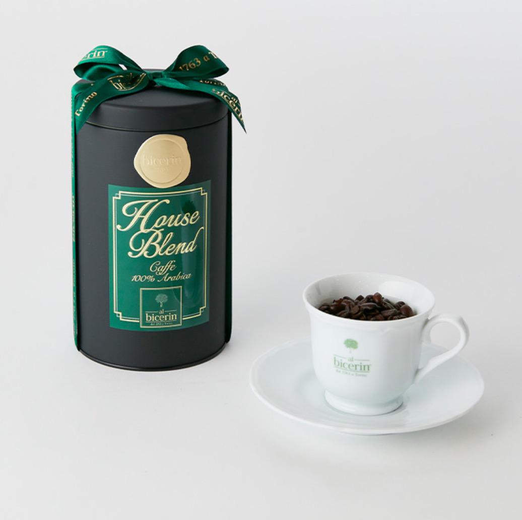 緑色のリボンがかかった黒い缶と白いコーヒーカップに入ったコーヒ豆