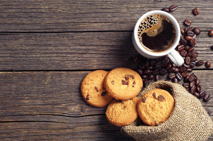 木製のテーブルに、コーヒー入りのマグカップとチョコチップクッキーが置かれている。