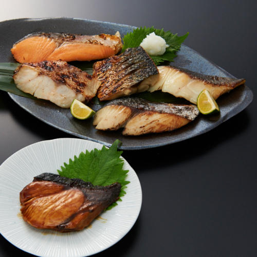 白色の皿にぶりの照焼きがのり、黒色の皿に5種の焼き魚がのっている。