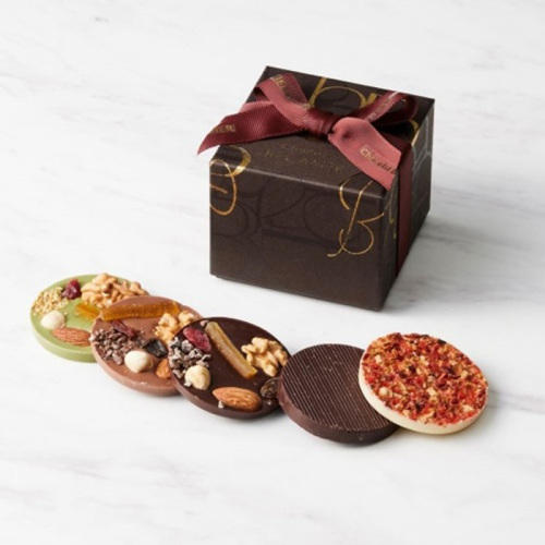 ナッツやドライフルーツなどがトッピングされた5種類の丸い板チョコレートと、リボンがついた茶色い化粧箱が置かれている