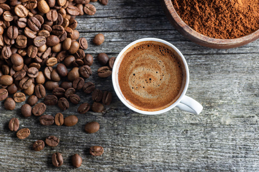 テーブルの中央にコーヒー入りのマグカップが置かれ、まわりにコーヒー豆と粉が置かれている。