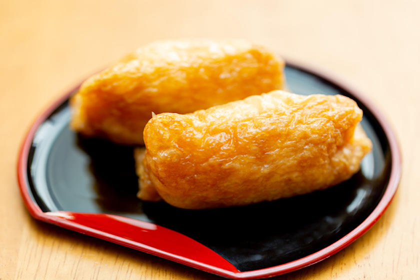 黒色の皿にいなり寿司が2個のっている。