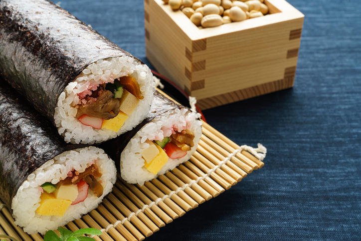巻きすの上に3本の太巻き寿司が置かれ、奥には豆が入った枡が添えられている。