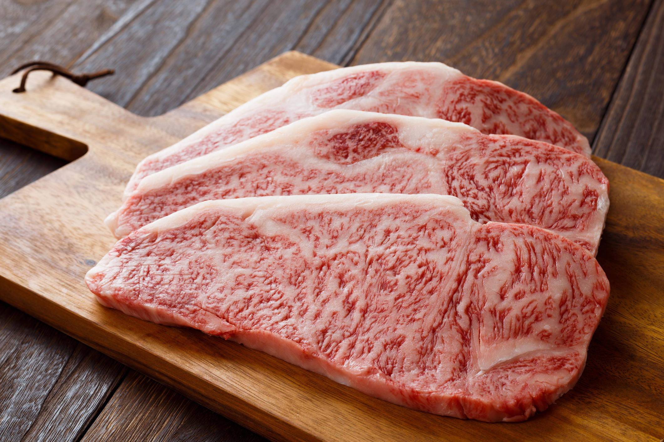 カッティングボードにのせたサーロインステーキ肉３枚
