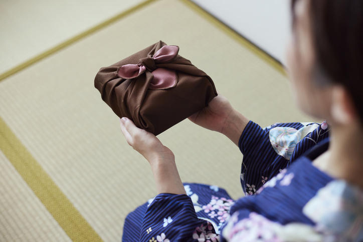 風呂敷に包まれた贈り物を両手で渡す着物の女性