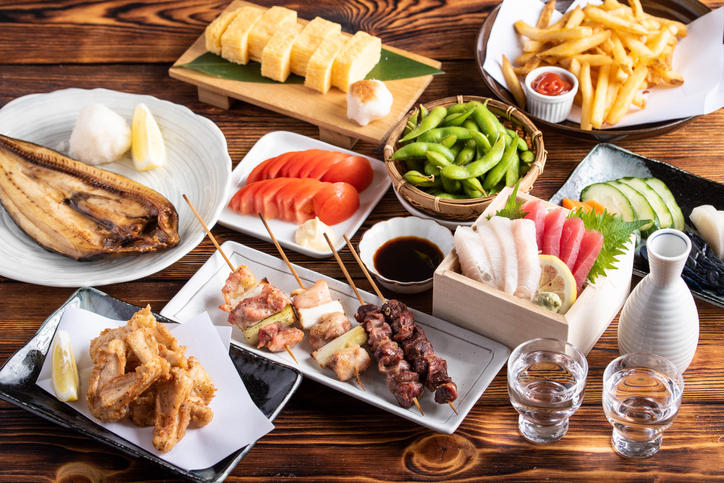 テーブルに日本酒と、焼き魚、卵焼き、枝豆などさまざまなおつまみが置かれている。