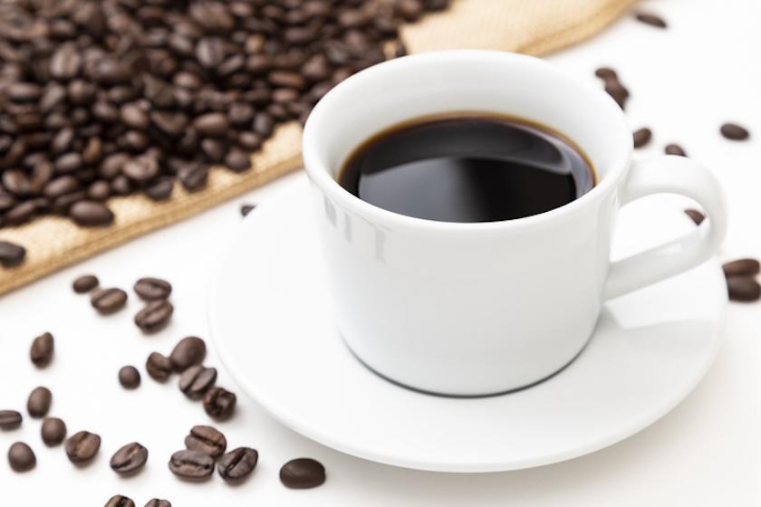 白い背景に、コーヒーの入ったカップ、コーヒー豆が置かれている。