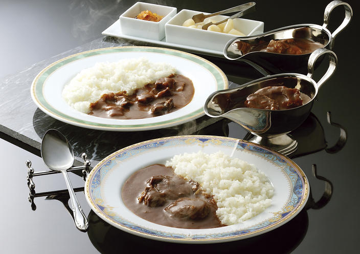 二つの平皿に盛られたカレーライスと銀のグレイビーボートに入ったカレー、白い四角いさらに盛られたらっきょう
