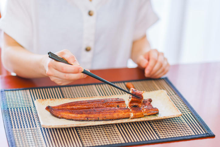 器に置かれたうなぎの蒲焼きを箸で持ち上げる様子
