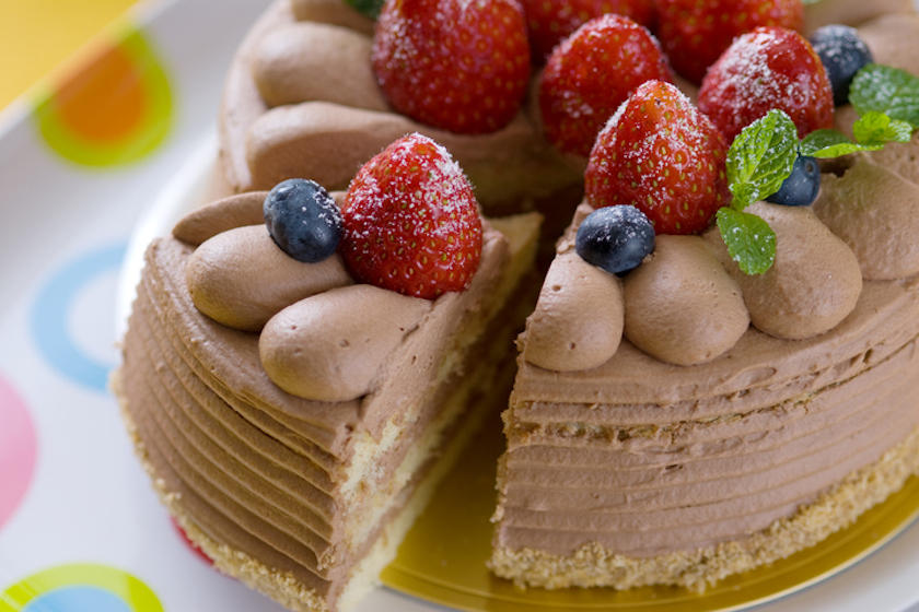 いちごとブルーベリーがのったチョコレートケーキを切り分けている。
