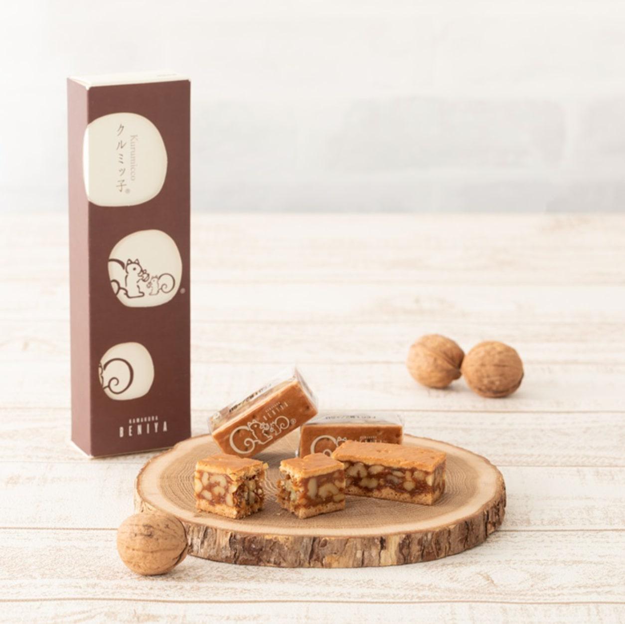 白い木目調のテーブルに置かれた木のトレーに乗った焼き菓子と茶色いボックスとくるみ
