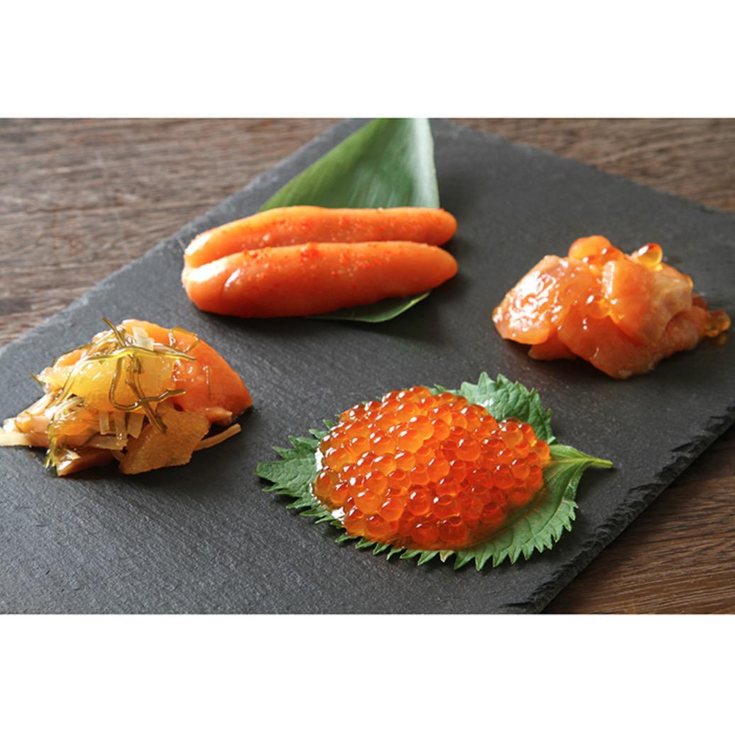 木製テーブルの上の黒い四角い皿にのった4種類の魚介類を使った惣菜