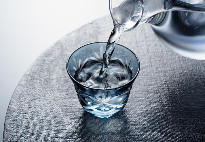 黒い背景に置かれた江戸切子の青いグラスに注がれた焼酎