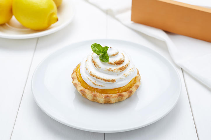 白いテーブルの上の白い丸皿に乗ったホイップクリームとミントがトッピングされた小さなレモンタルト