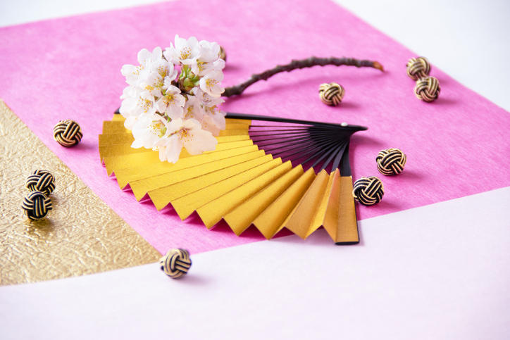 ピンクの和紙の上に置かれた金色の扇子と桜の小枝