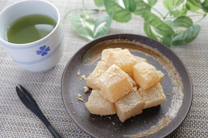 茶色い丸皿に盛られたわらび餅と湯呑みに入れられた緑茶