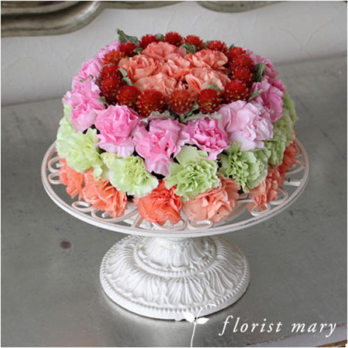 アンティーク調の花器にのったケーキのようなスプレーカーネーションやいちご草