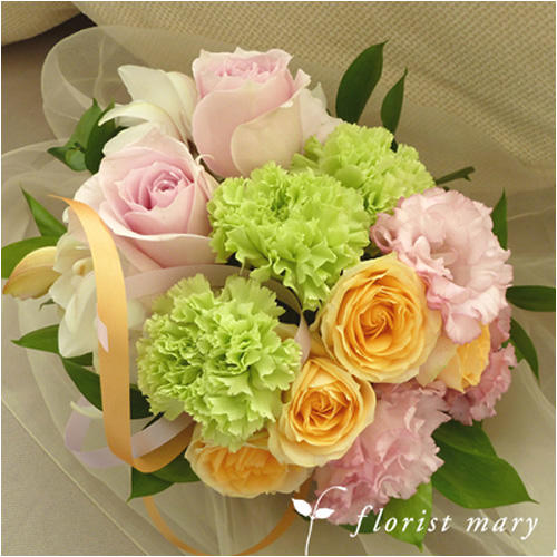 白い布の上のパステル系の花束（ピンクと黄色のバラ、緑のカーネーションなど）