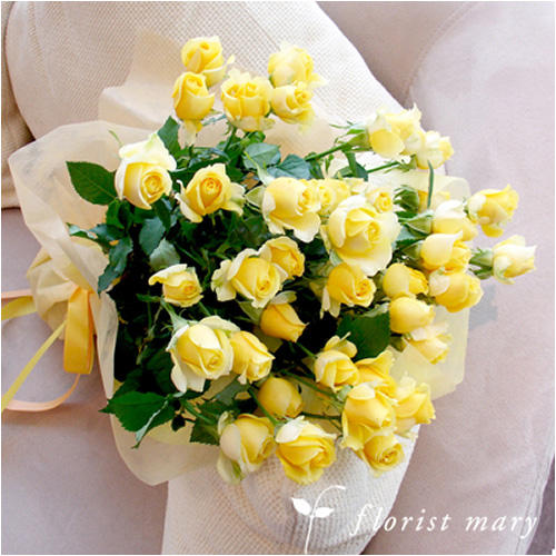 白い布張りソファの上の黄色いバラ数十本の花束