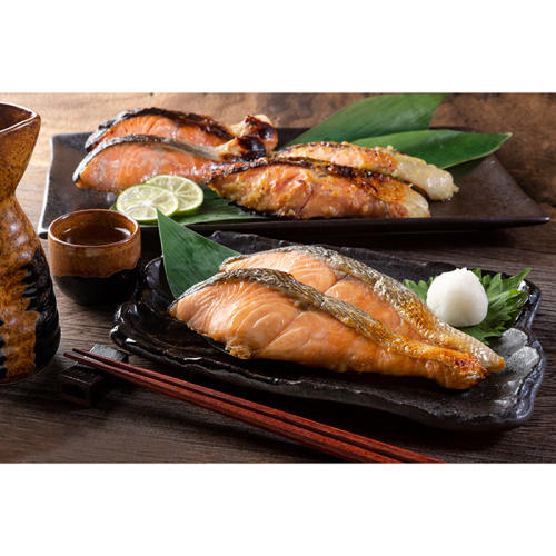 焼鮭が盛られた黒い皿が、木のテーブルの上に並べられている