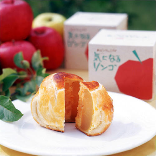 まるごと1個のりんごが入ったアップルパイが、白い丸皿の上に置かれており、その奥には、「気になるリンゴ」と書かれた箱と、りんごが数個置かれている