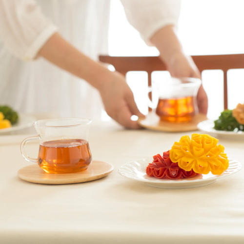白い服の人がテーブルに『花咲かりん』と紅茶の入ったカップを並べている