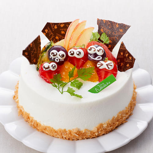 生クリームをぬったデコレーションケーキに顔が描かれた葡萄やフルーツがトッピングされている