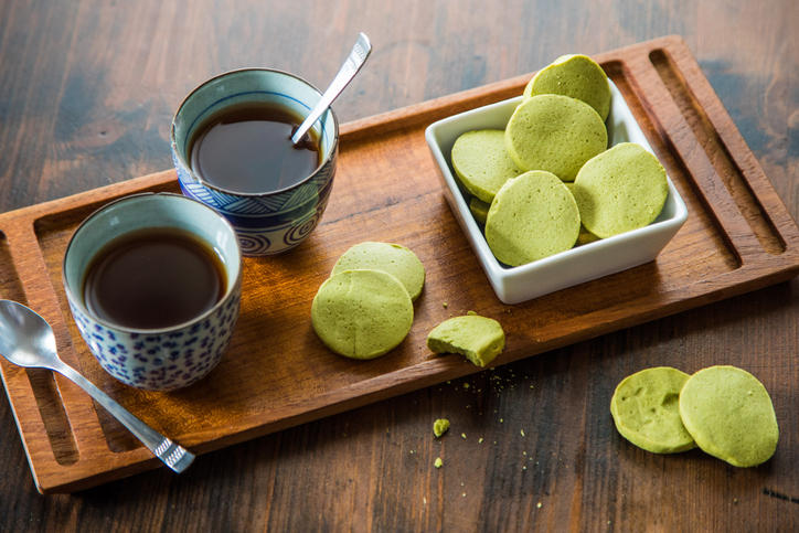 茶色い木のお盆に乗せられたお茶入りの湯呑みと抹茶のクッキー