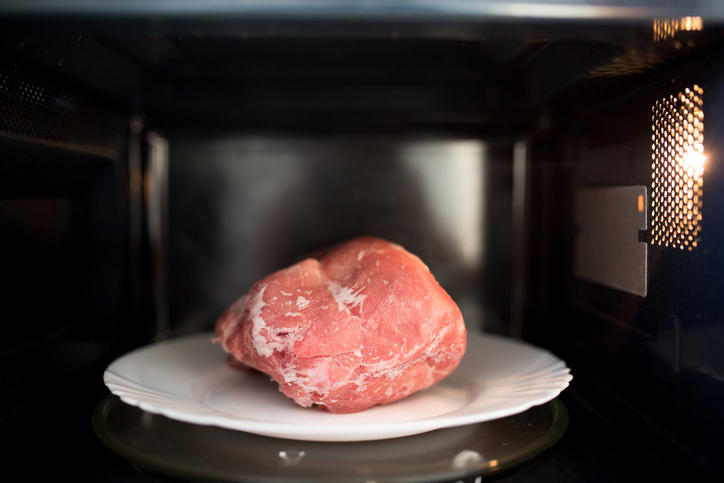 電子レンジの中の白い丸皿の上の凍った肉の塊