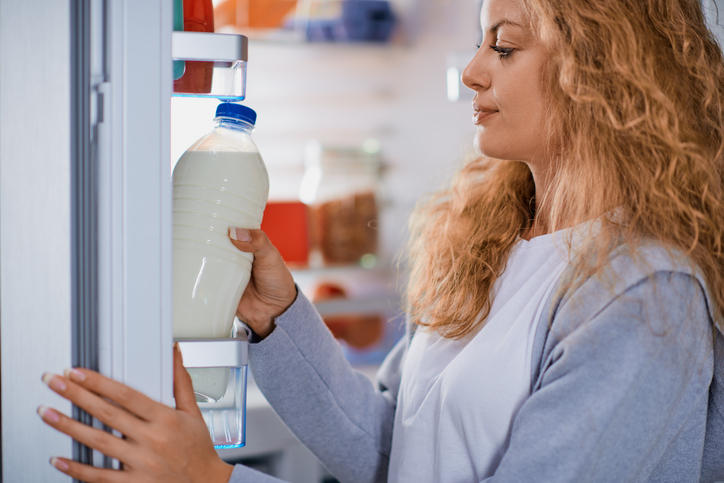 ブロンズヘアーの女性が冷蔵庫に牛乳をしまっている