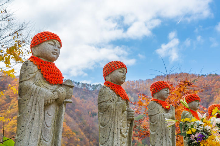 空と山並みを背景に並ぶ赤い帽子の4体のお地蔵さん