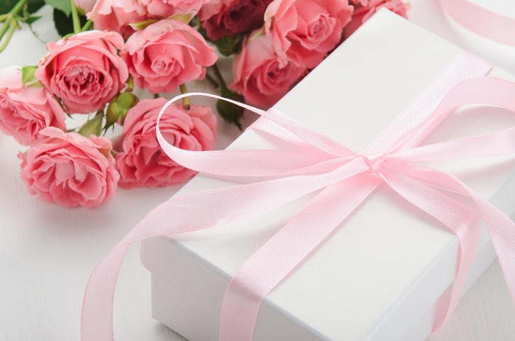 ピンクのリボンがついた白いギフトボックスと、ピンクのバラの花束