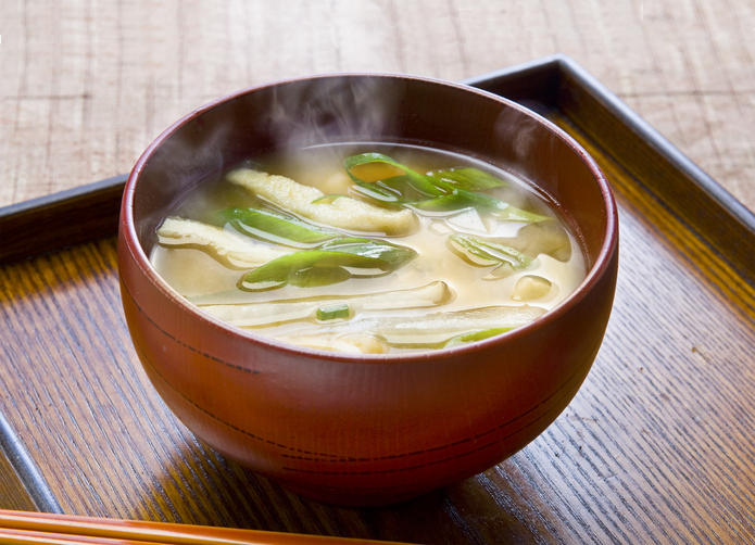 木製トレーの上の赤い汁椀に入った油揚げとネギの味噌汁