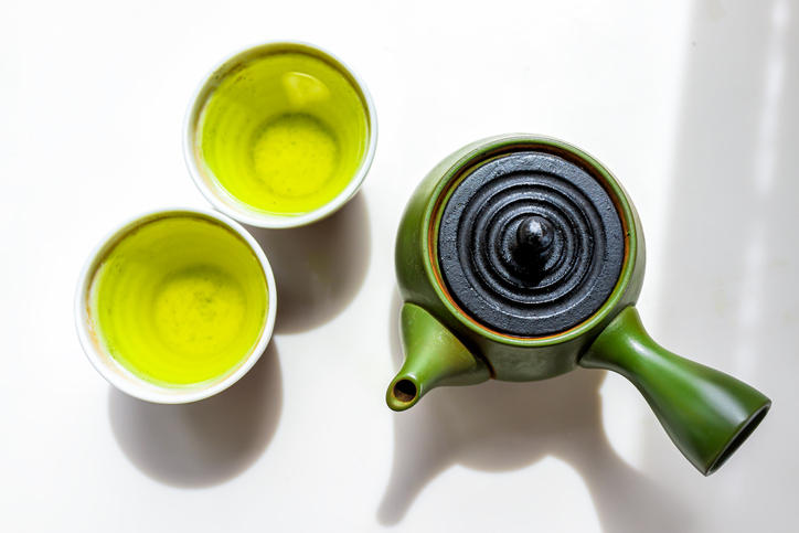 白いテーブルに置かれた緑色の急須とお茶入りの2個の湯呑